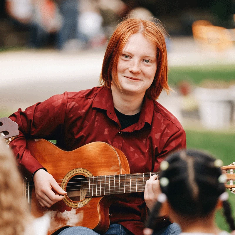 Eine junge Person spielt Gitarre und lächelt.