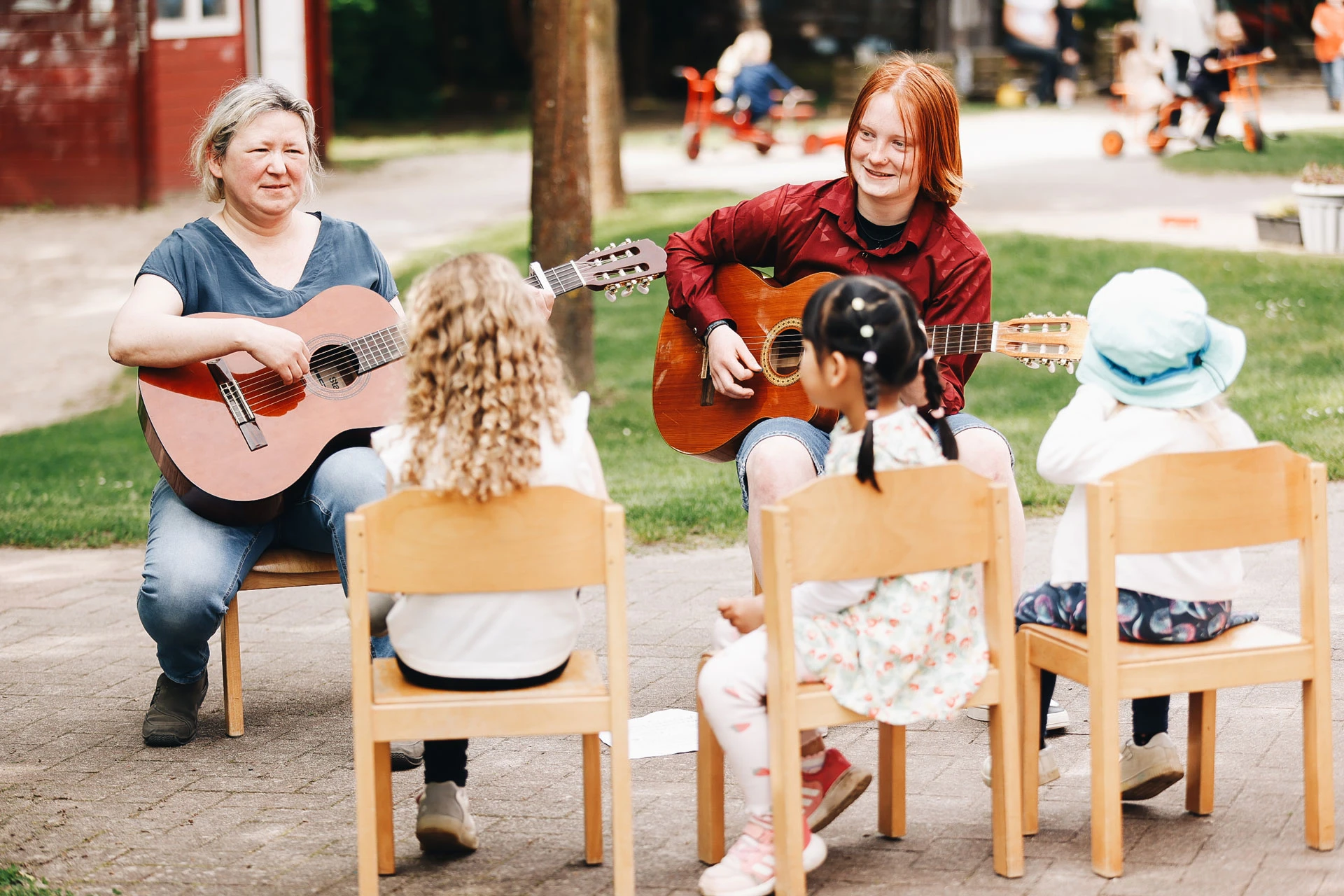 Zwei Peronen sitzen vor Kindern und spielen Gitarre und singen.